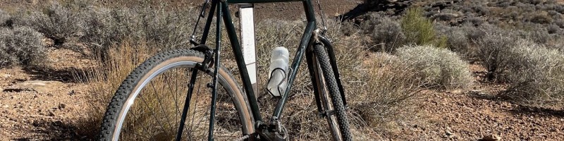 Dark green steel gravel bike with brown bar tape standing in the desert outside St. George, Utah