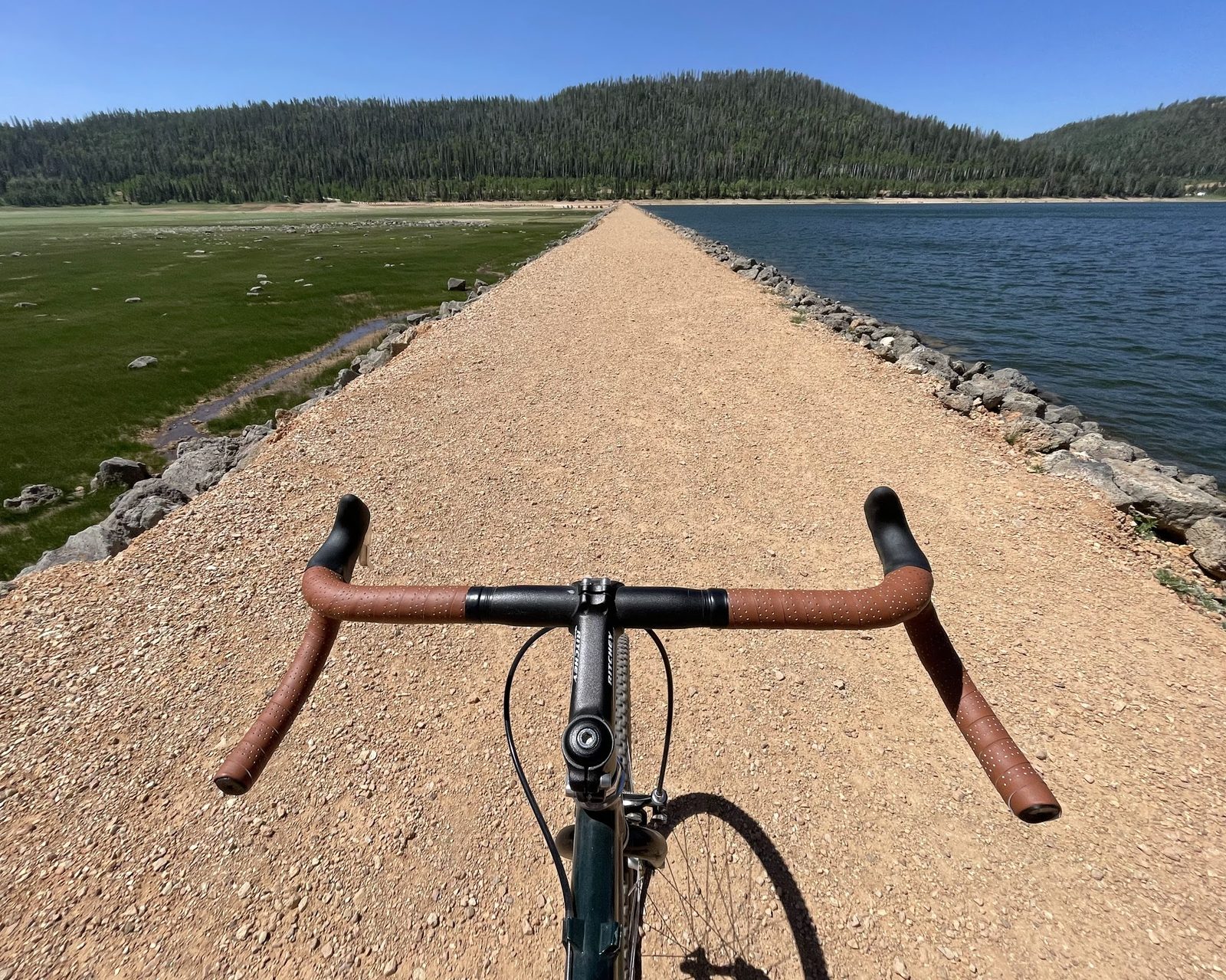 Riding view over the brown drop bars on a gravel causeway beside a lake